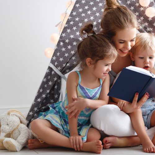 family mother reading to children book in tent at home